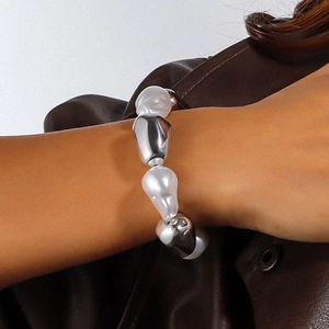 Details eines klobigen Silber- und Perlenarmbands über einer braunen Lederjacke getragen