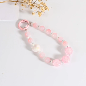 Detail of pink beaded phone charm with heart pendant and rose beads on white background