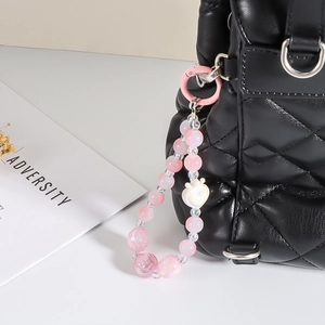 Detailed view of pink beaded phone charm with heart pendant on a black quilted bag
