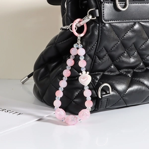 Pink beaded phone charm with heart and flower pendants on a black quilted bag