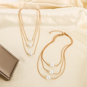 Detail of layered gold necklaces with white pearls on elegant champagne silk fabric