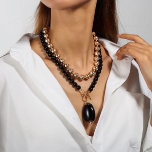 Detail of layered beaded necklace with black oval pendant and golden metal toggle clasp