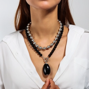 Detail of double-layer beaded necklace featuring a large black teardrop pendant on a model