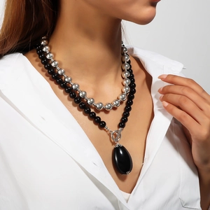 Detail of layered silver and black beaded necklace with a water drop pendant on model