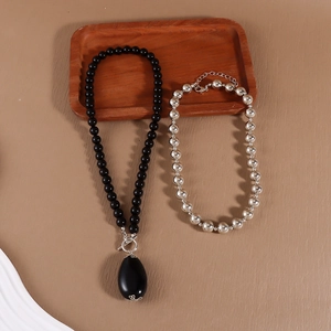 Macro detail of beaded necklace set featuring black matte beads and silver teardrop pendant