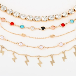 Detalle de set de 5 tobilleras doradas con circonitas de colores y colgantes de rayos
