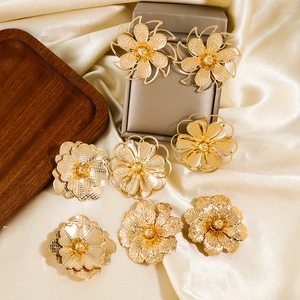 Detailansicht verschiedener großer goldener Blumenohrringe auf champagnerfarbener Seide
