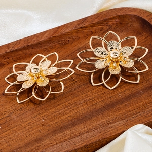 Detail goldener geschichteter Blumenohrringe mit hohlen Blütenblättern auf weißer Seide