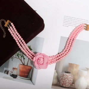 Detail van een drielaagse roze parelketting met stoffen roos op een fluwelen sieradendoosje