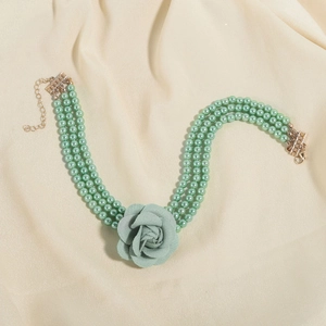 Detail van meerlaagse groene parelketting met stoffen roos en gouden karabijnsluiting