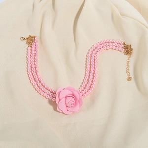Detail van drie lagen roze parelsnoeren met een stoffen camelia bloem en gouden sluiting