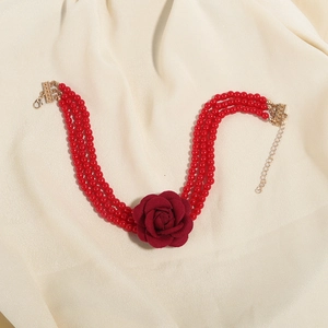 Detail van drielaagse rode kralenketting met een grote stoffen roos en gouden sluiting