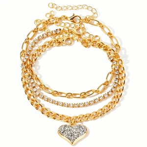 Set bracciale e cavigliera d'oro multistrato con ciondolo a cuore in strass su sfondo bianco