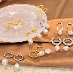 Elegant stainless steel pearl earrings collection displayed on brown silk fabric and marble tray