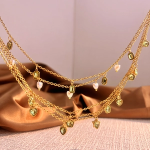 Elegante gouden laagjesketting met smaragd zirkoon en hartparels op zijden stof