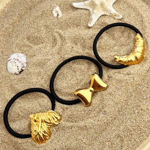Lot de trois chouchous noirs avec pendentifs dorés en métal sur un décor de plage ensoleillé