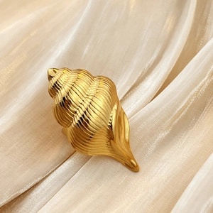 Anello a conchiglia dorato in acciaio inossidabile su sfondo di seta champagne