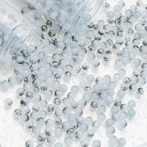 Blue glass beads with gold speckles spilling from bottles on a white textured surface