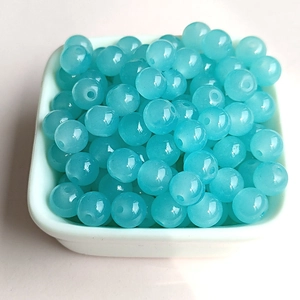 Detailed macro view of light blue translucent glass beads stacked in a white ceramic dish