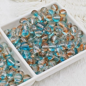 Détail macro de perles en verre dégradé bleu et orange dans un plateau de rangement blanc