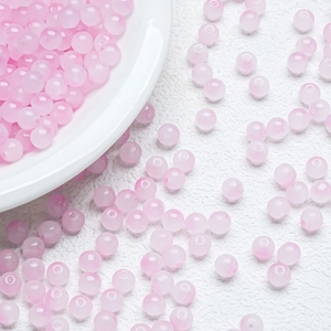 Macro shot of 8mm pink jelly glass beads for DIY jewelry making on a white textured background