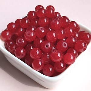 Close-up of deep red translucent 8mm glass beads in a white bowl for DIY jewelry making