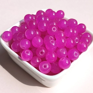 Close-up of polished magenta round glass beads for DIY jewelry making in a white dish