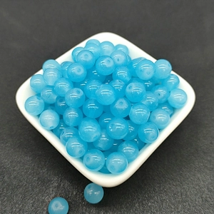 Close-up of translucent blue glass beads for DIY jewelry making on white ceramic plate