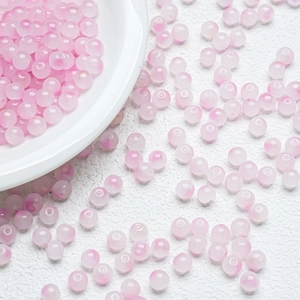 Detailed view of pink gradient glass beads scattered on a textured white surface