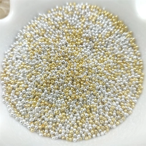Close-up of gold and silver metallic round spacer beads in a white ceramic bowl