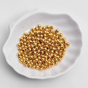 Golden round metal spacer beads for DIY jewelry making displayed in a white shell bowl