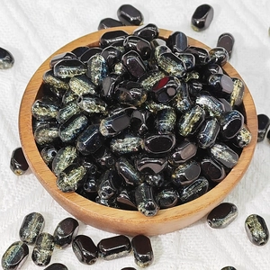 Macro view of 6x10mm black and gold lampwork glass beads in a wooden bowl for DIY jewelry