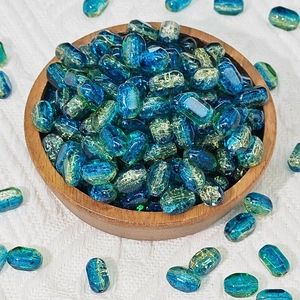 Close-up of blue glass lampwork beads with gold foil in a wooden bowl on white fabric