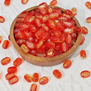 Macro view of rectangular red glass beads with gold foil in a wooden bowl for DIY jewelry