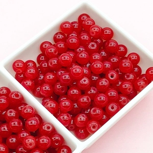 Close-up of vibrant red translucent glass beads in a white tray for DIY jewelry making