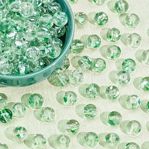 Close-up of green and white floral glass beads with central drill holes for DIY jewelry