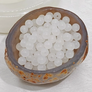 Close-up of translucent white chalcedony glass beads in a natural stone bowl for DIY
