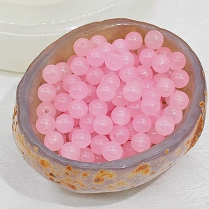 Close-up of translucent pink round glass beads in a textured natural stone bowl for DIY jewelry