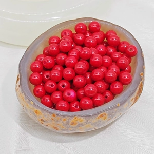 Macro shot of bright red glass beads with drill holes in a textured stone bowl