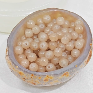 Detail view of semi-transparent beige agate round beads in a natural stone bowl