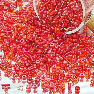 Macro view of assorted red glass seed beads pouring out for DIY jewelry making