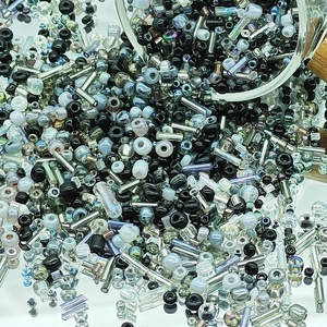 Macro shot of mixed black and silver glass seed beads pouring onto a reflective surface