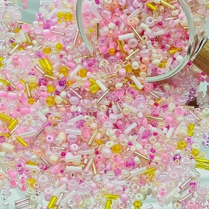 Dynamic close-up of mixed pink and yellow DIY glass beads pouring from a glass container