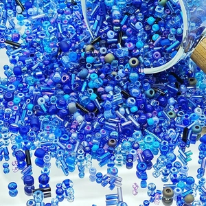 Detailed macro view of assorted blue glass seed beads spilling from a glass bottle