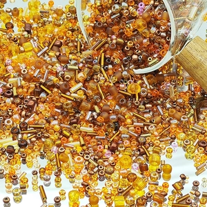 Mixed warm tone DIY glass seed beads and bugle beads spilling from a glass jar