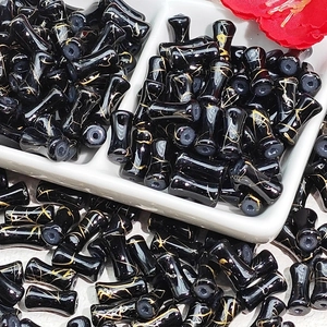 Macro view of black glass bamboo-style beads with gold textures in a white tray