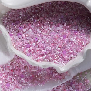 Close-up of mixed pink and purple glass seed beads and bugle beads in a ceramic dish