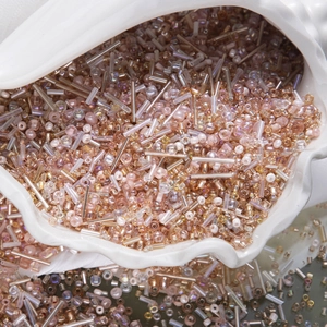 Macro shot of mixed pink and rose gold glass seed beads in a shell container