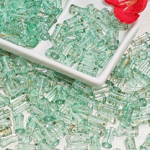 Macro shot of light green cylinder glass beads with gold texture in a ceramic tray