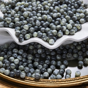 Gros plan de perles en pierre naturelle marbrée gris et vert sur un plateau en céramique